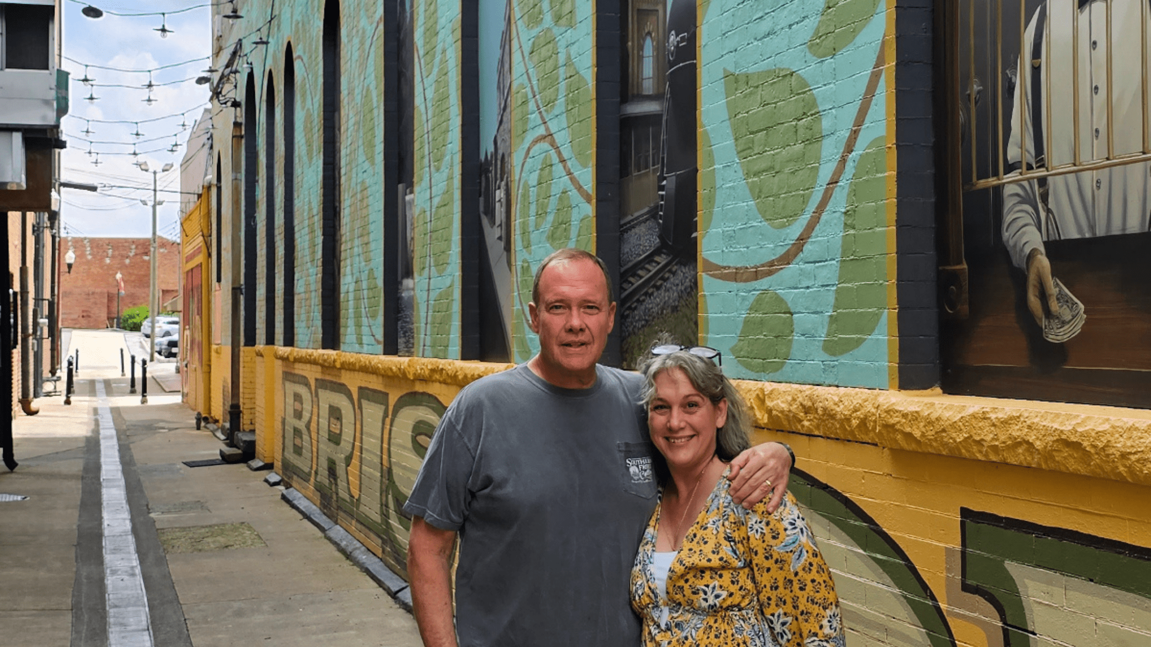 Things to Do in Bristol TN VA: What to See, Eat & Explore in 2025 5 Kathy and Steve smiling in front of colorful downtown Bristol TN VA murals—capturing one of the best things to do in Bristol TN VA for art lovers and photo seekers.