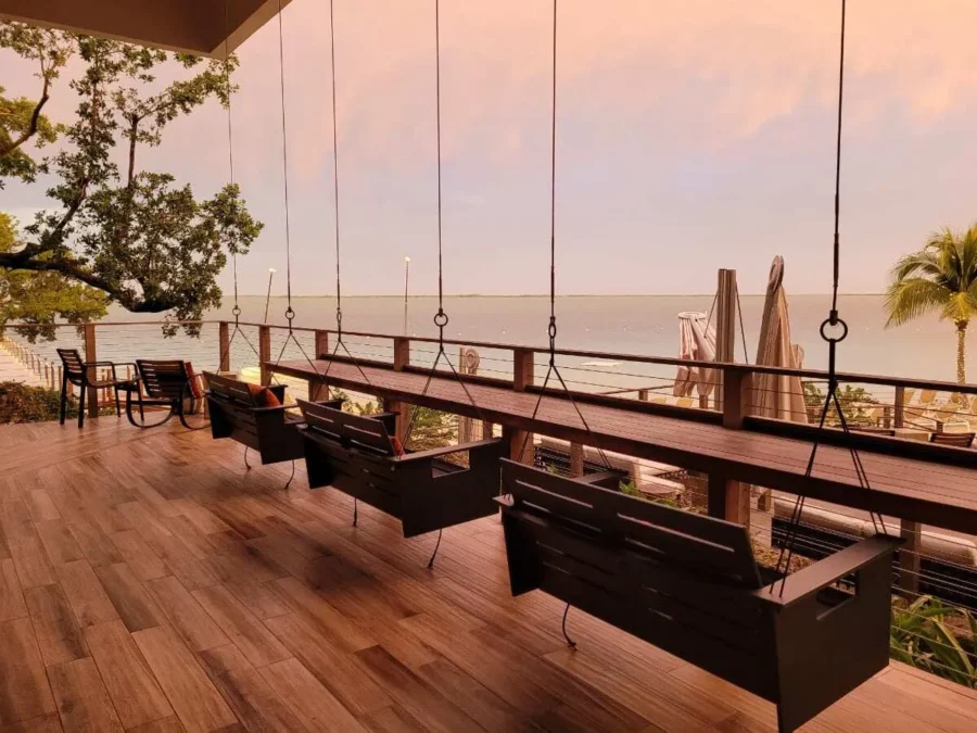 Baker's Cay Resort Key Largo review 2 Wooden porch swings overlooking the ocean at sunset on a deck at Baker’s Cay Resort in Key Largo, Florida, with palm trees, lounge chairs, and a peaceful waterfront view in the distance.