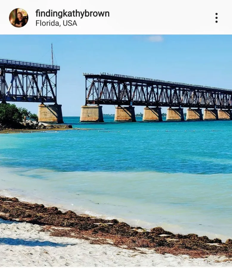 Is Bahia Honda Worth It? Hereโs Why We Say Yes 1 Old railroad bridge over turquoise water at Bahia Honda State Park in Florida, with white sand and seaweed in the foreground under a clear blue sky.