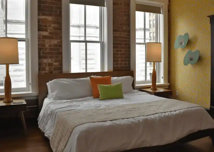 Quirky, Cool, and Totally Chattanooga: Inside The Dwell Hotel (Review) 3 Stylish guest room at The Dwell Hotel in Chattanooga, TN featuring exposed brick, modern lamps, retro wallpaper, and a cozy king bed with colorful accent pillows. Review