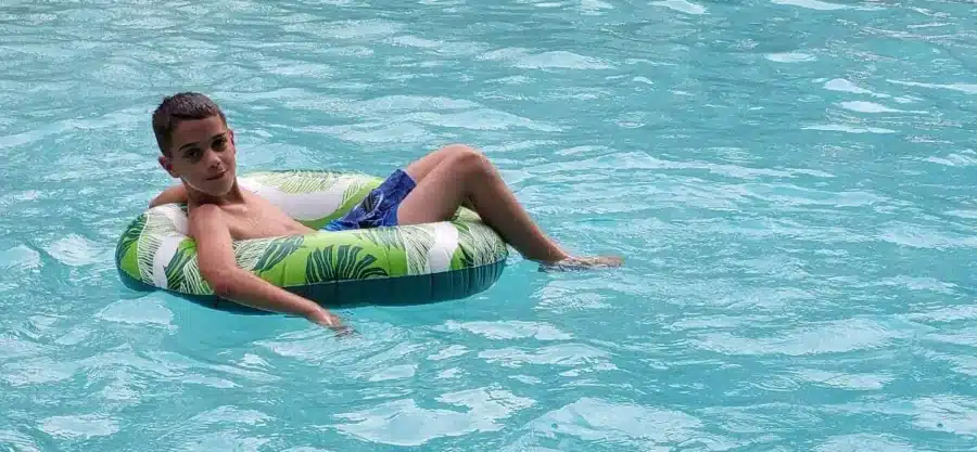 11 Best Hotels in Orlando with Lazy River (No Theme Park Required) 2 Young boy relaxing on a green and white inflatable tube in a lazy river at a hotel pool in Orlando, Florida—perfect for family and multigenerational travel.