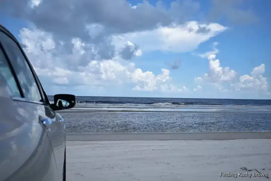 The Best Drive on the Beach in Jacksonville FL: Huguenot Memorial Park 4 A silver car parked on the white sand at Huguenot Memorial Park with a view of the Atlantic Ocean and a cloudy blue sky in Jacksonville, FL β a beach you can drive on.