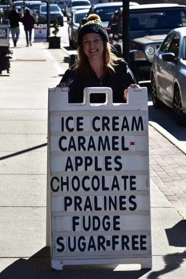 The Best Things to Do in Bryson City, NC 7 Kathy Brown standing in downtown Bryson City, North Carolina in front of a sweets shop sign โ highlighting local treats as one of the fun things to do in Bryson City North Carolina.