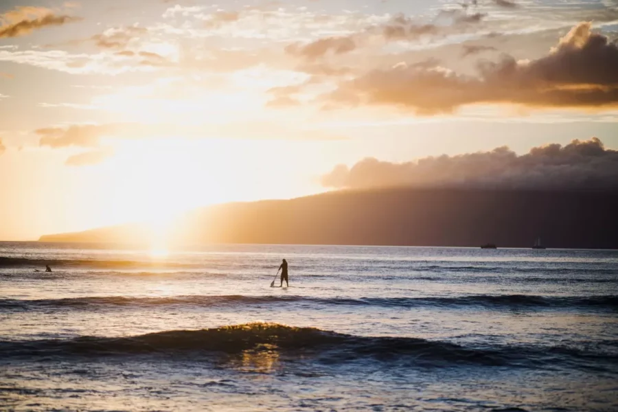 Person paddleboarding at sunrise on calm ocean waters near Melbourne, Florida with golden light and soft waves]
