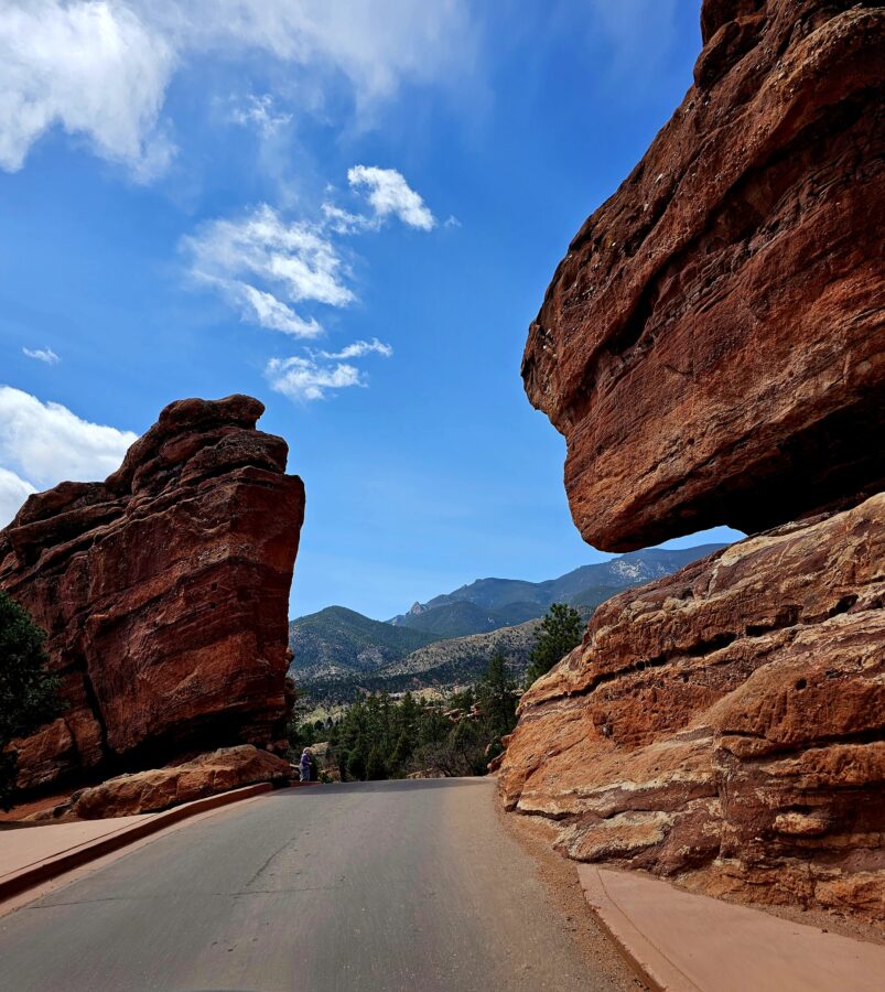 A No-Hike Way to See Garden of the Gods: Scenic Drive Tips for Older Travelers 9 Road winding through massive red rock formations at Garden of the Gods in Colorado, with blue sky and distant mountain views.