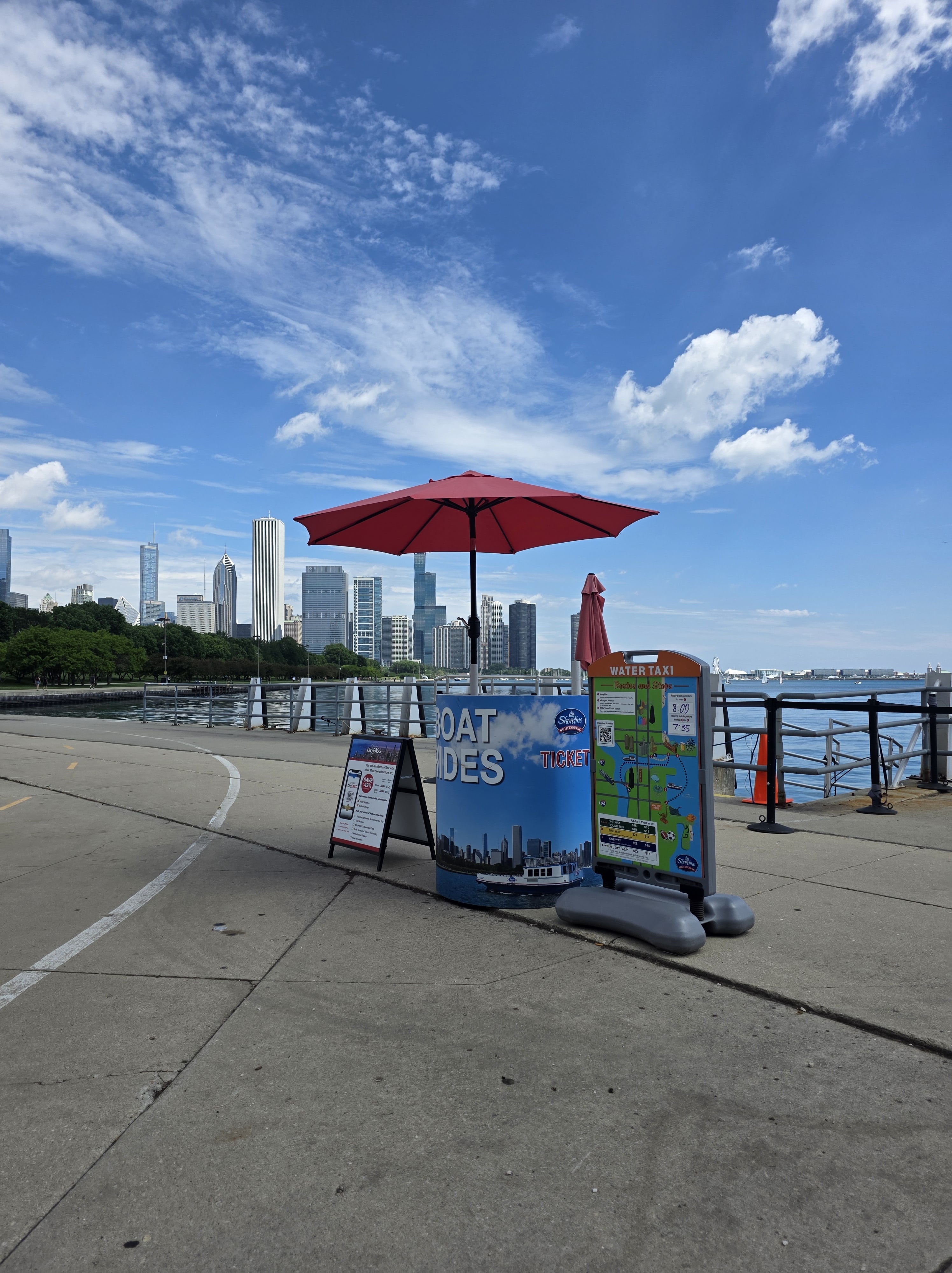 Easy Guide to The Chicago Water Taxi Stops 3 Shoreline Sightseeing ticket stand with a red umbrella near the Museum Campus water taxi stop, overlooking Lake Michigan and Chicago skyline.